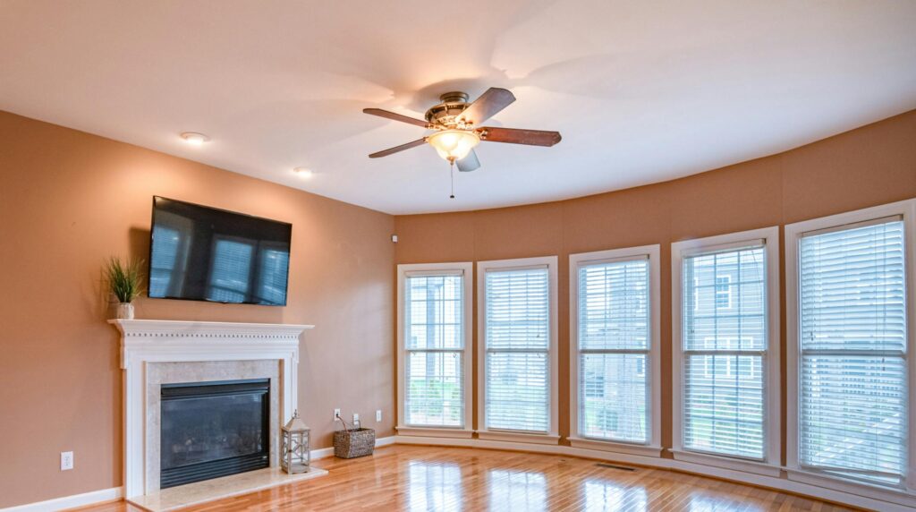 Bright living room with hardwood floors, fireplace, TV, and ceiling fan.
