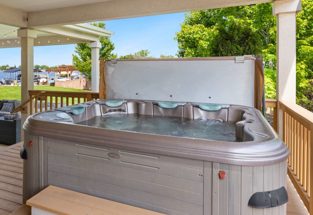 Explore a serene outdoor patio featuring a luxurious hot tub overlooking a tranquil lake.